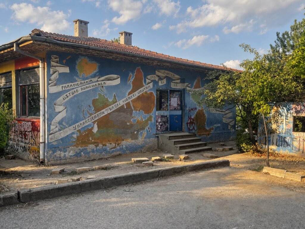 Blue mural of a world map painted on the exterior wall of a METU student building, with Turkish text banners reading political and philosophical slogans.