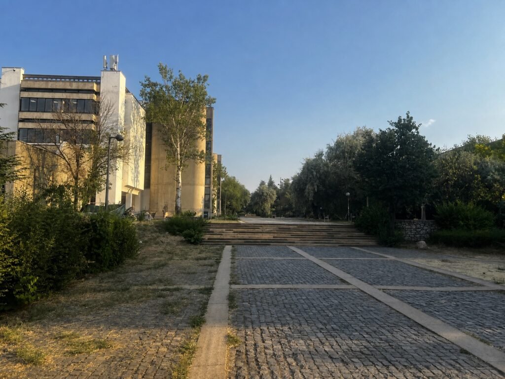 METU university building beside a cobblestone path and staircase, surrounded by trees under a clear evening sky.