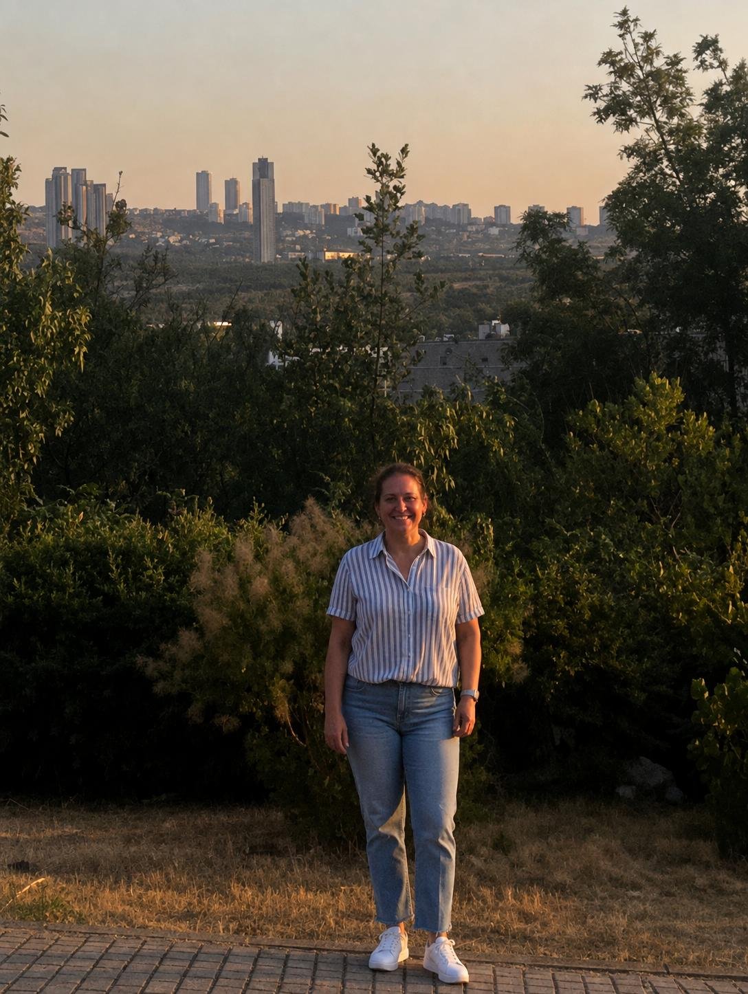 Tiffany standing at a scenic overlook on the ODTÜ campus in Ankara at sunset, with the city skyline and green hills in the background.