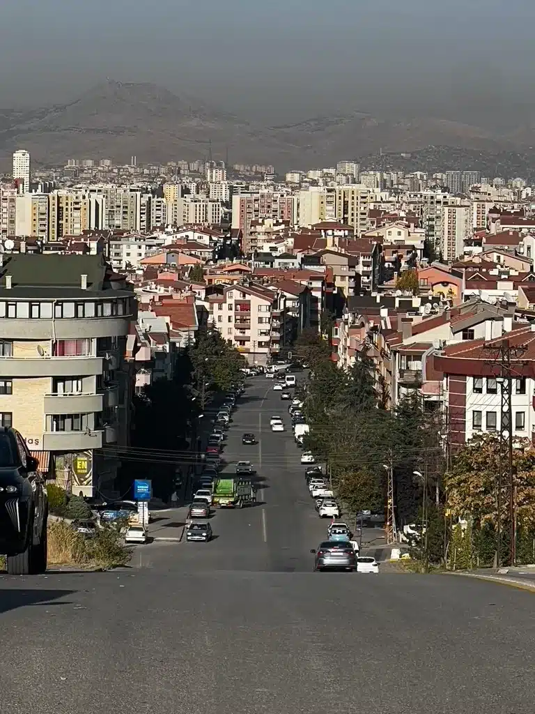 A steep street descends between Ankara apartment buildings toward the city and distant hills.