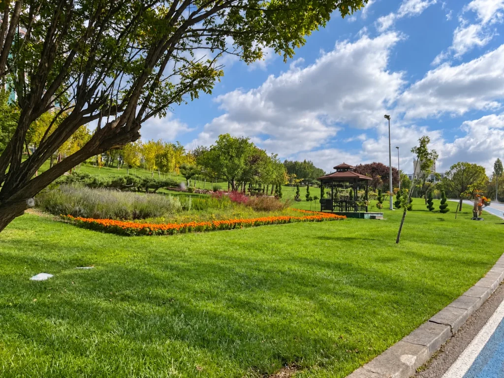 A wooden gazebo stands beyond a curved border of orange flowers and a broad green lawn.