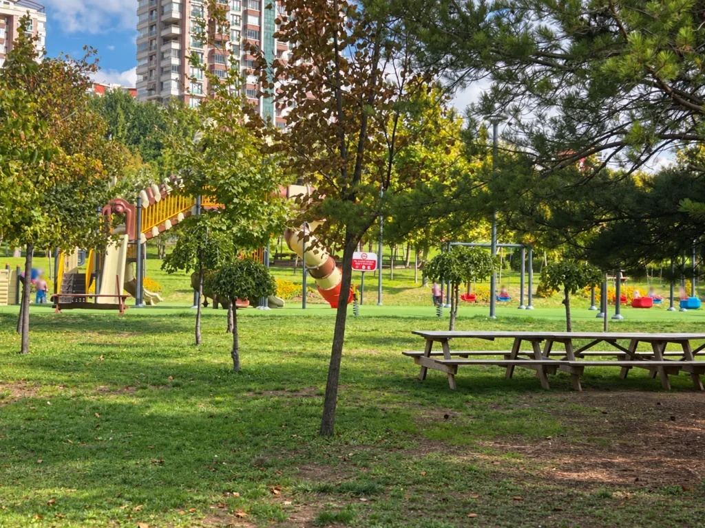 Slides and swings stand among trees behind picnic tables at 30 Ağustos Zafer Parkı.