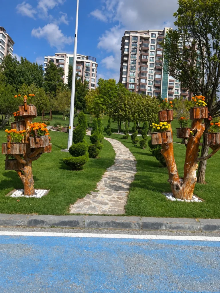 A narrow stone path winds between wooden flower planters and sculpted shrubs beneath apartment buildings.