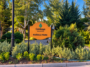 Kuğulu Park entrance sign surrounded by lush green trees and landscaped plants in Ankara, Türkiye.