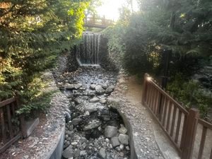 Small waterfall flowing beneath a wooden bridge among trees and rocks in Kuğulu Park, Ankara.