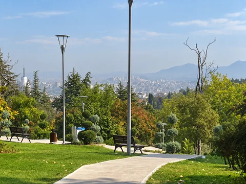 A curving park path and benches overlook Ankara's hazy skyline beyond the trees.
