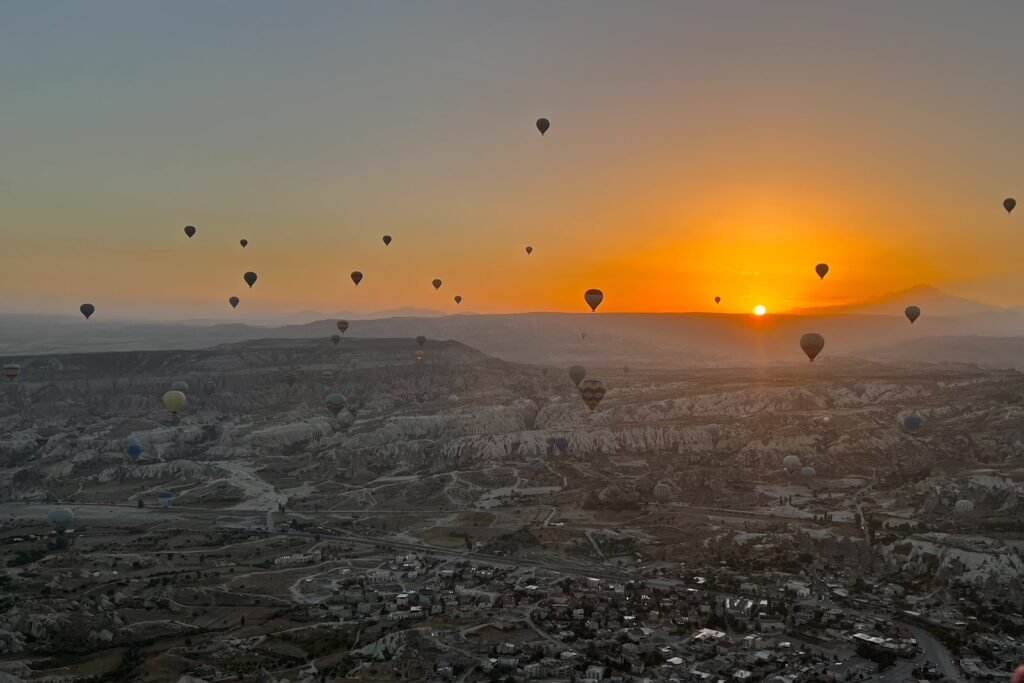 Hot-air balloons floating over Cappadocia at sunrise above the valleys and towns of central Türkiye.