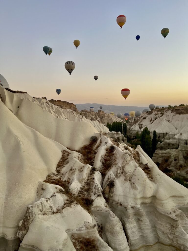 Hot-air balloons floating above the pale rock valleys of Cappadocia at sunrise in Türkiye.