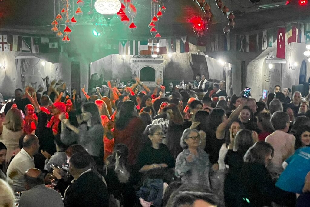 Crowded Turkish Night performance with colorful stage lighting and flags in Cappadocia, Türkiye.