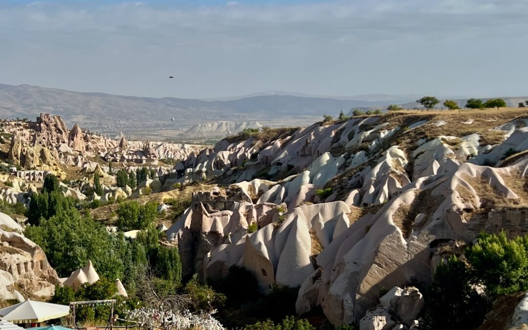 Wide Cappadocia valley with fairy chimneys, rock formations, greenery, and a distant hillside settlement in Türkiye