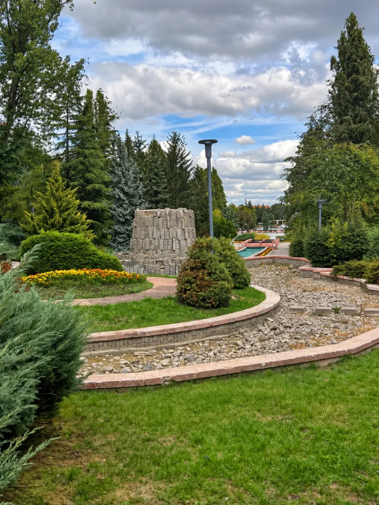 Yellow and orange flowers beside a curved stone-lined channel with stepping stones and tall conifers in Dikmen Vadisi.