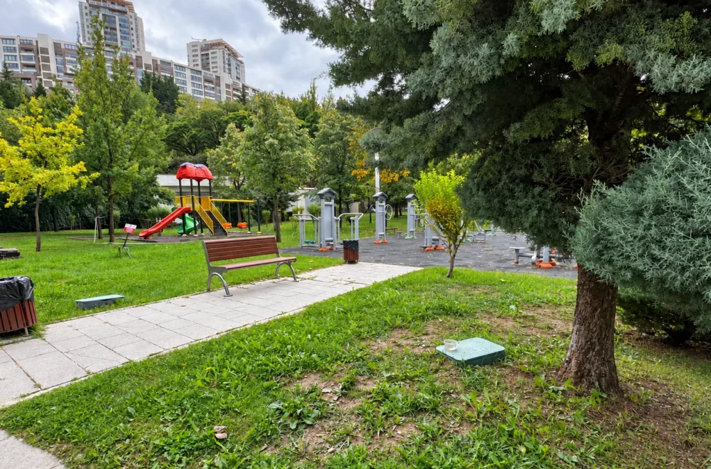 Colorful playground slide and outdoor exercise machines beside a bench and trees in Dikmen Vadisi.
