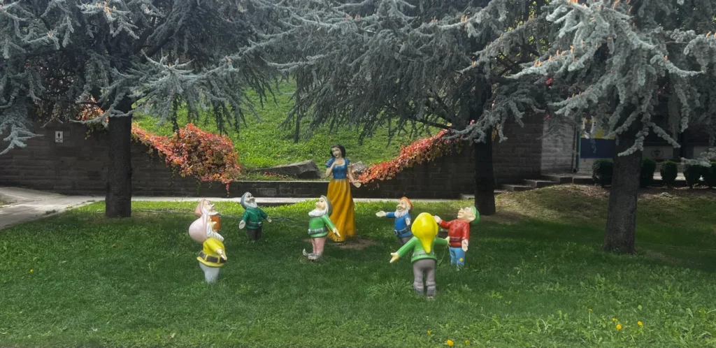 Snow White and dwarf statues arranged on grass beneath evergreen trees in Dikmen Vadisi.