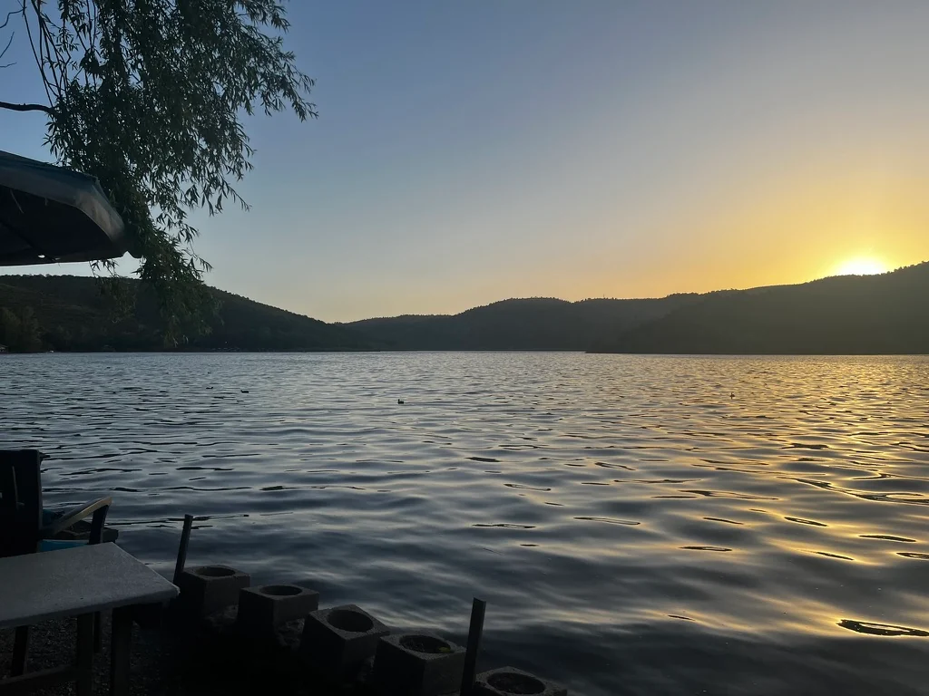 The setting sun glows above dark hills and casts golden reflections across Lake Eymir, framed by overhanging branches.
