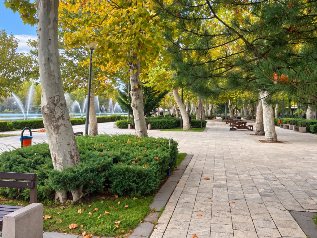 A shaded path runs past picnic tables and mature trees beside spraying fountains in Gençlik Parkı.