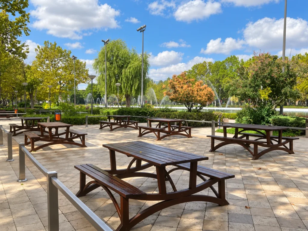 Wooden picnic tables stand in dappled shade beside trees and fountains at Gençlik Parkı.