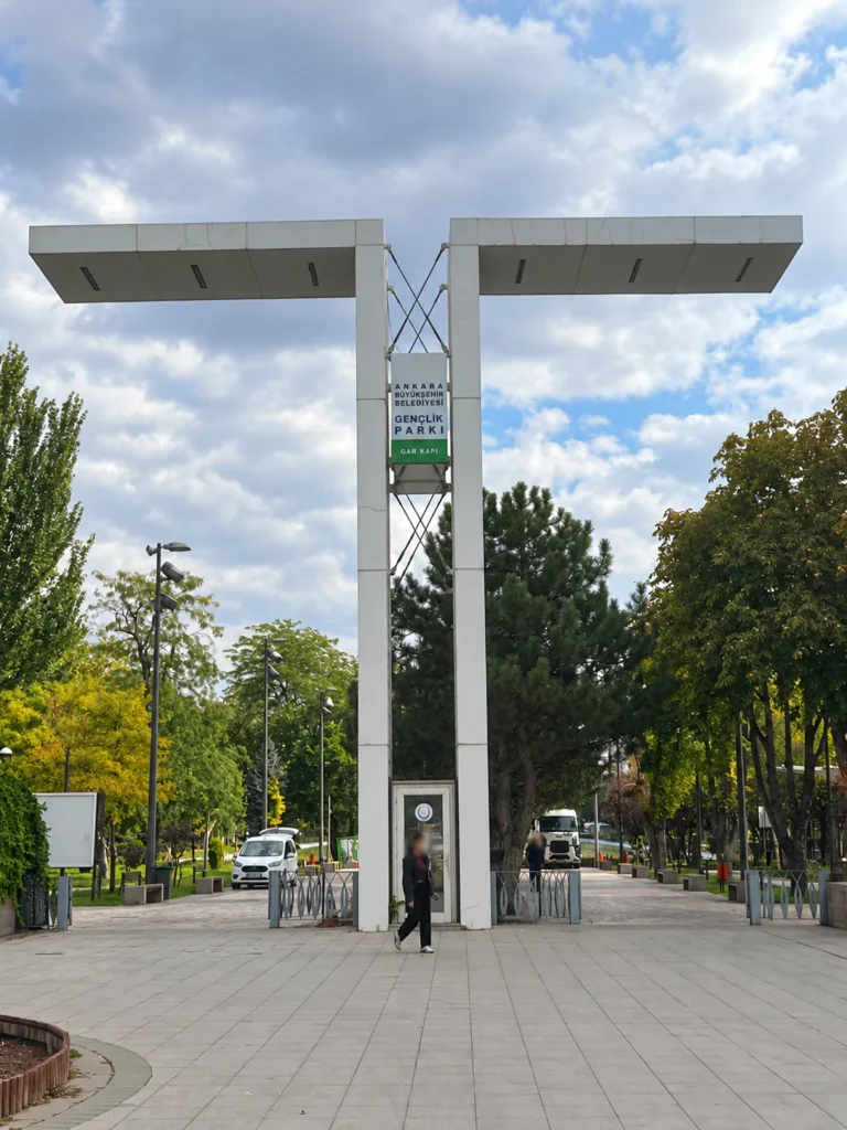 A tall white gateway marked Gençlik Parkı Gar Kapı stands above a paved entrance among trees.