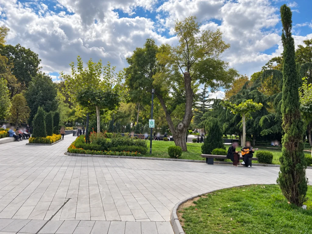 Paved paths curve past flower beds, benches, and tall trees in Güvenpark, Ankara.