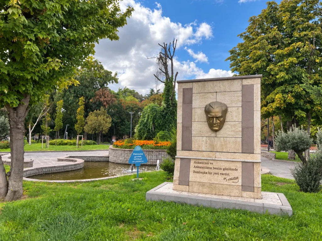 An Atatürk portrait relief and Turkish inscription stand beside a pond and orange flowers in Kurtuluş Parkı.
