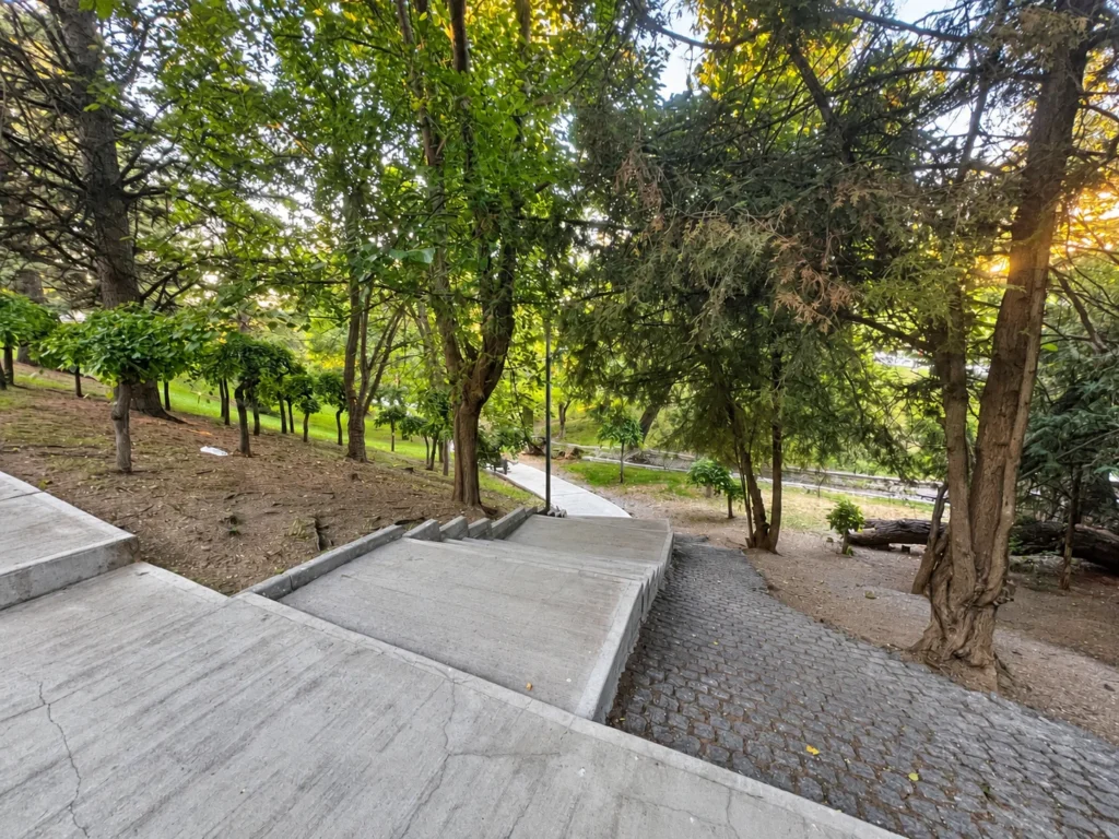 Wide concrete steps descend through mature trees beside a cobbled slope in Seğmenler Parkı.
